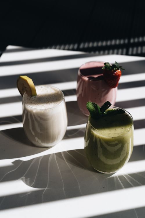 Free Three smoothie glasses with lemon, strawberry, and mint garnished in artistic lighting and shadows. Stock Photo