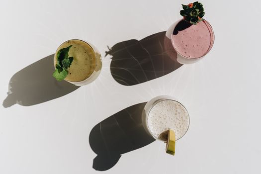 Top-down view of three diverse smoothies casting artistic shadows on a bright surface.