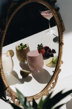 Artistic display of colorful fruit smoothies in an ornate mirror reflection with sunlight casting shadows.