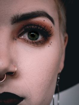 A detailed close-up of a person's face with piercings and striking eye makeup.