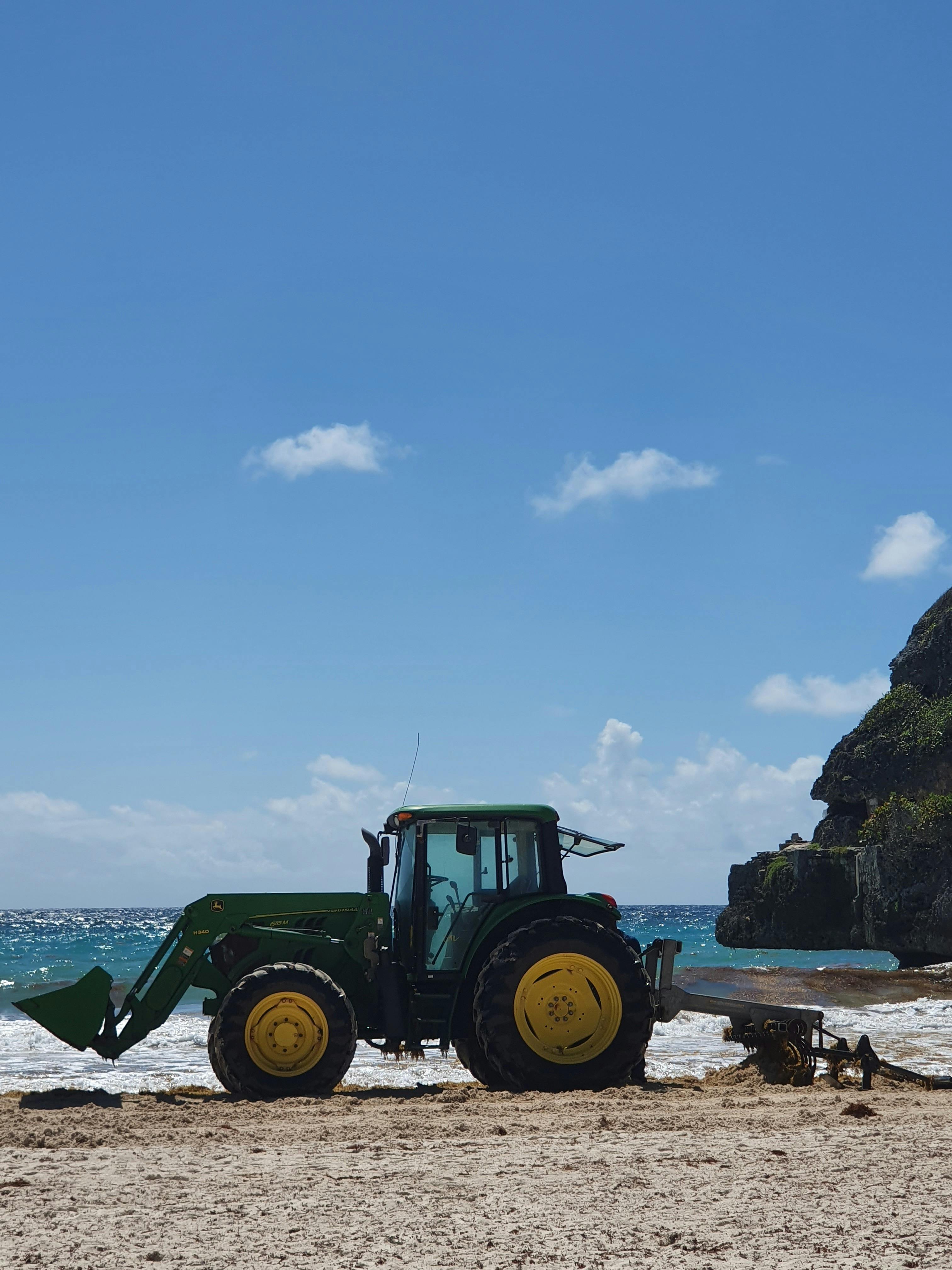 Beach cleaning tractor near rocky ocean on sunny day · Free Stock Photo