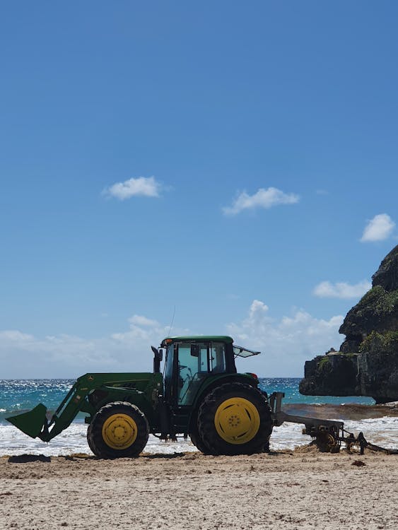 Beach cleaning tractor near rocky ocean on sunny day
