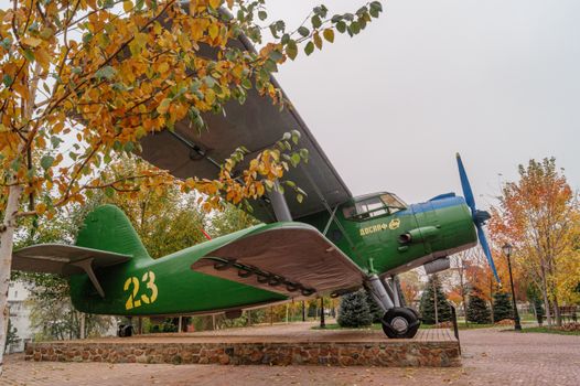 Vintage green airplane displayed in a park with autumn foliage creating a colorful backdrop.