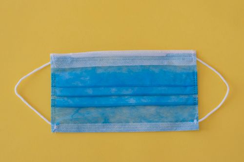 Free Close-up of a blue surgical mask on a vibrant yellow background highlighting health and protection. Stock Photo