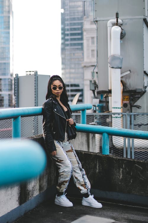 Woman in Black Leather Jacket and Jogger Pants Standing Beside Blue Metal Railings