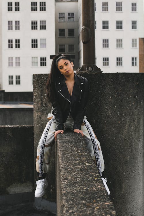 Woman in Black Leather Jacket Sitting on Concrete Wall