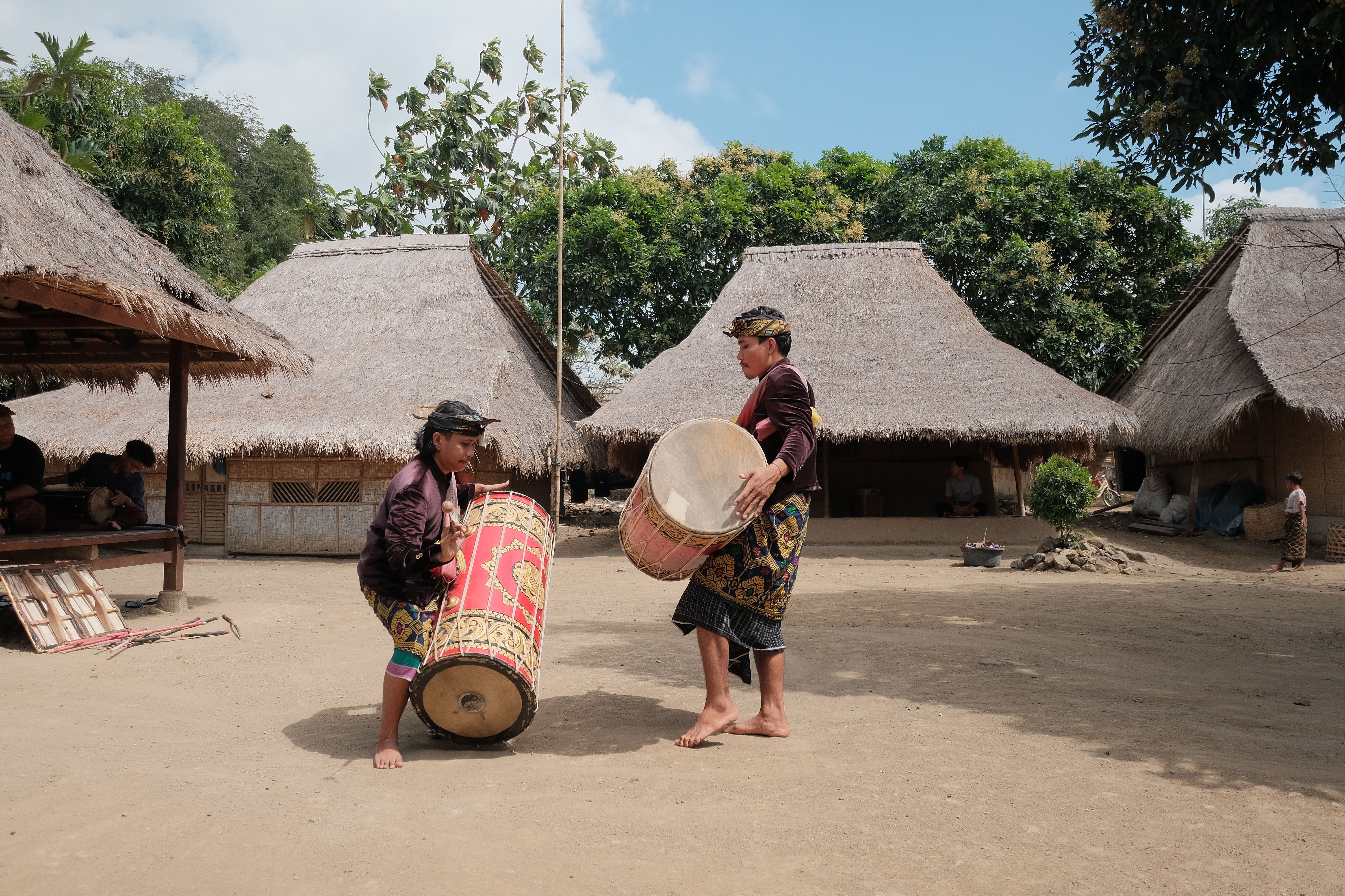 Musicians playing traditional drums in a village setting, showcasing cultural heritage.