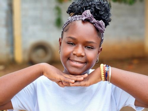 Free A cheerful young girl posing with her hands beneath her chin outdoors. Stock Photo