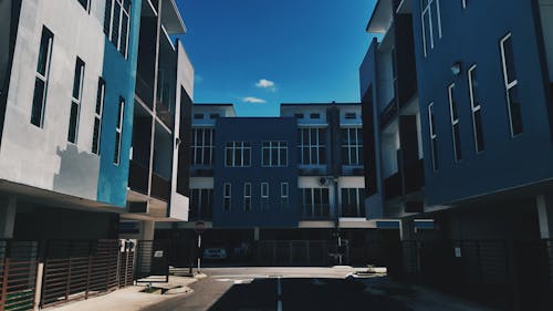 From below complex of simple modern geometric buildings with blue facade and balconies located on empty street of city district