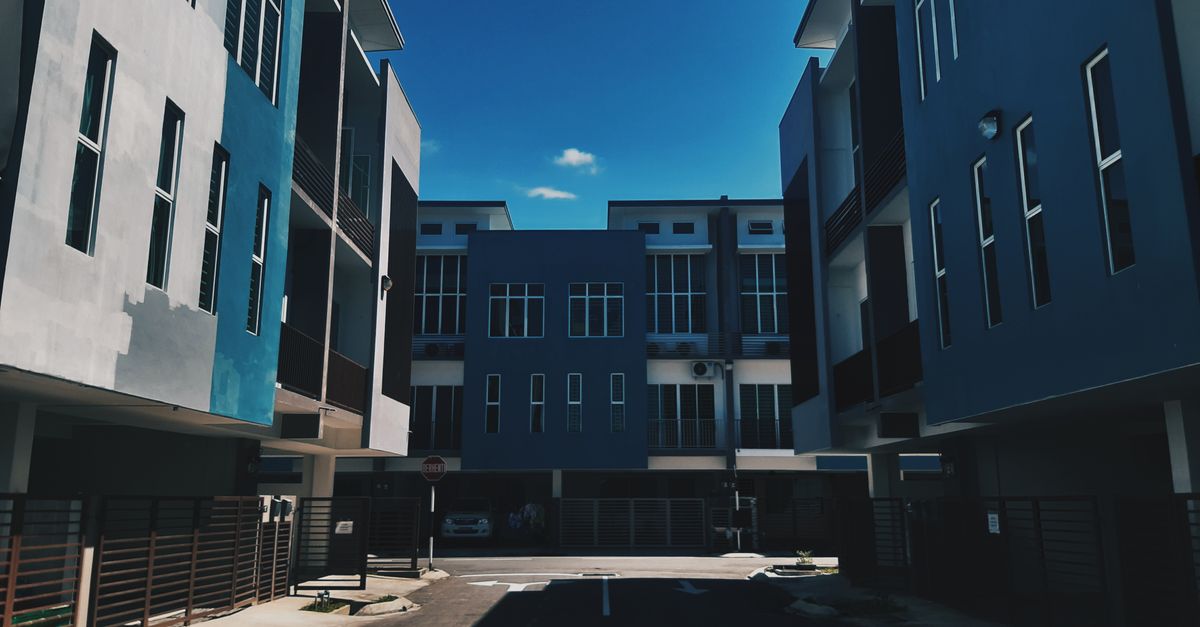From below complex of simple modern geometric buildings with blue facade and balconies located on empty street of city district
