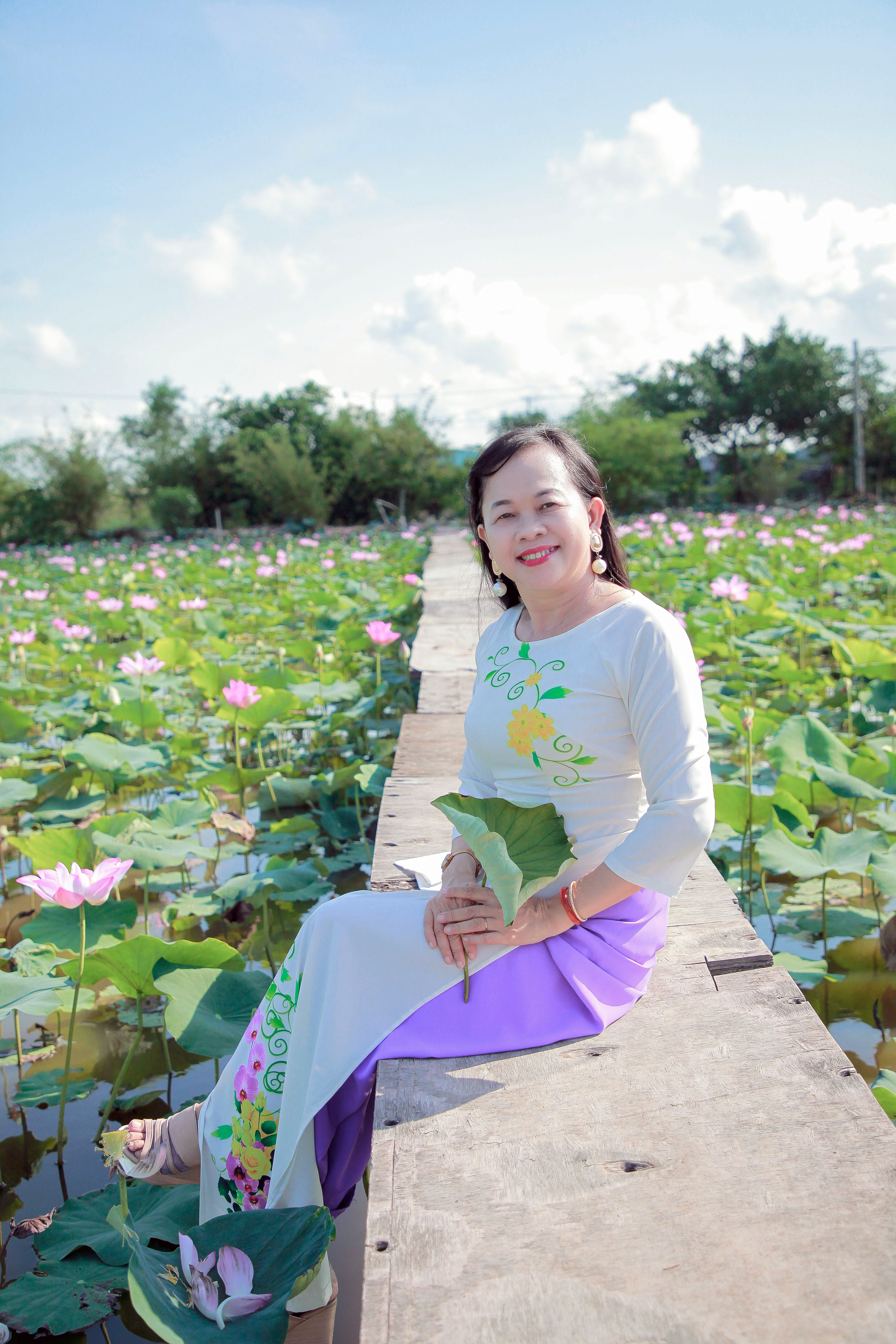 Elegant Woman Sitting Amidst Lotus Flowers in Sunlight · Free Stock Photo