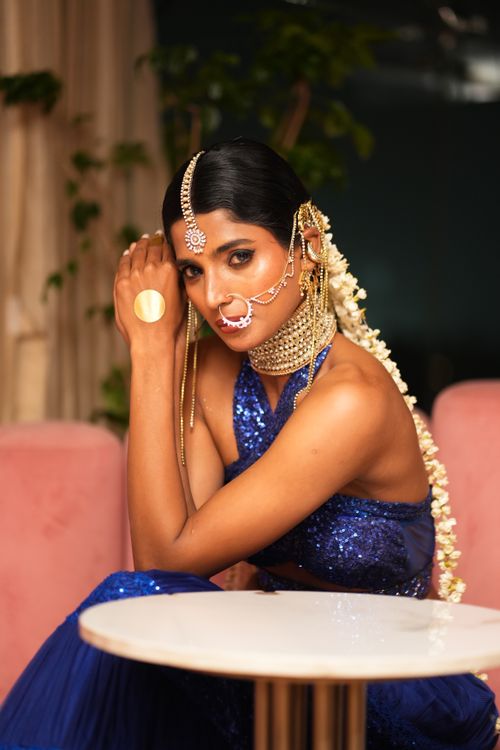 Free A woman in traditional Indian attire poses elegantly indoors with intricate jewelry and a blue dress. Stock Photo