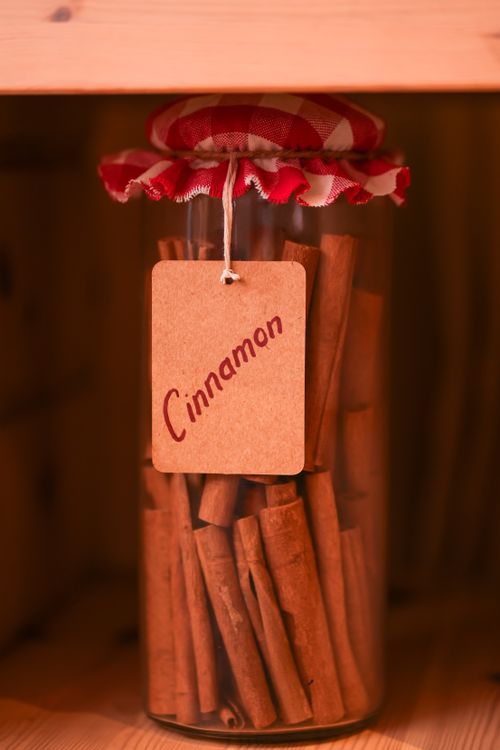 Free A decorative jar filled with cinnamon sticks, sealed with a gingham-patterned lid, and labeled 'Cinnamon'. Stock Photo