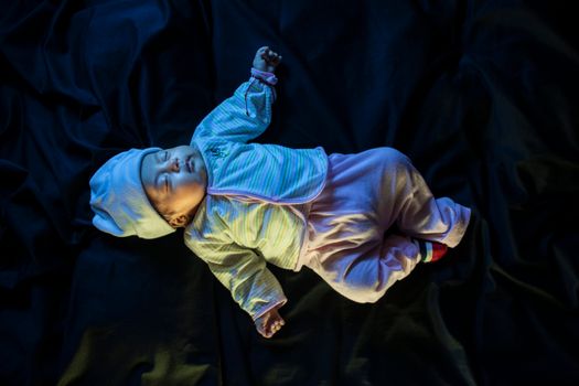 一个可爱的婴儿穿着色彩缤纷的衣服，在黑暗的表面上安然入睡