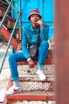 Fashionable person in a denim outfit sitting on industrial stairs, showcasing casual street style.