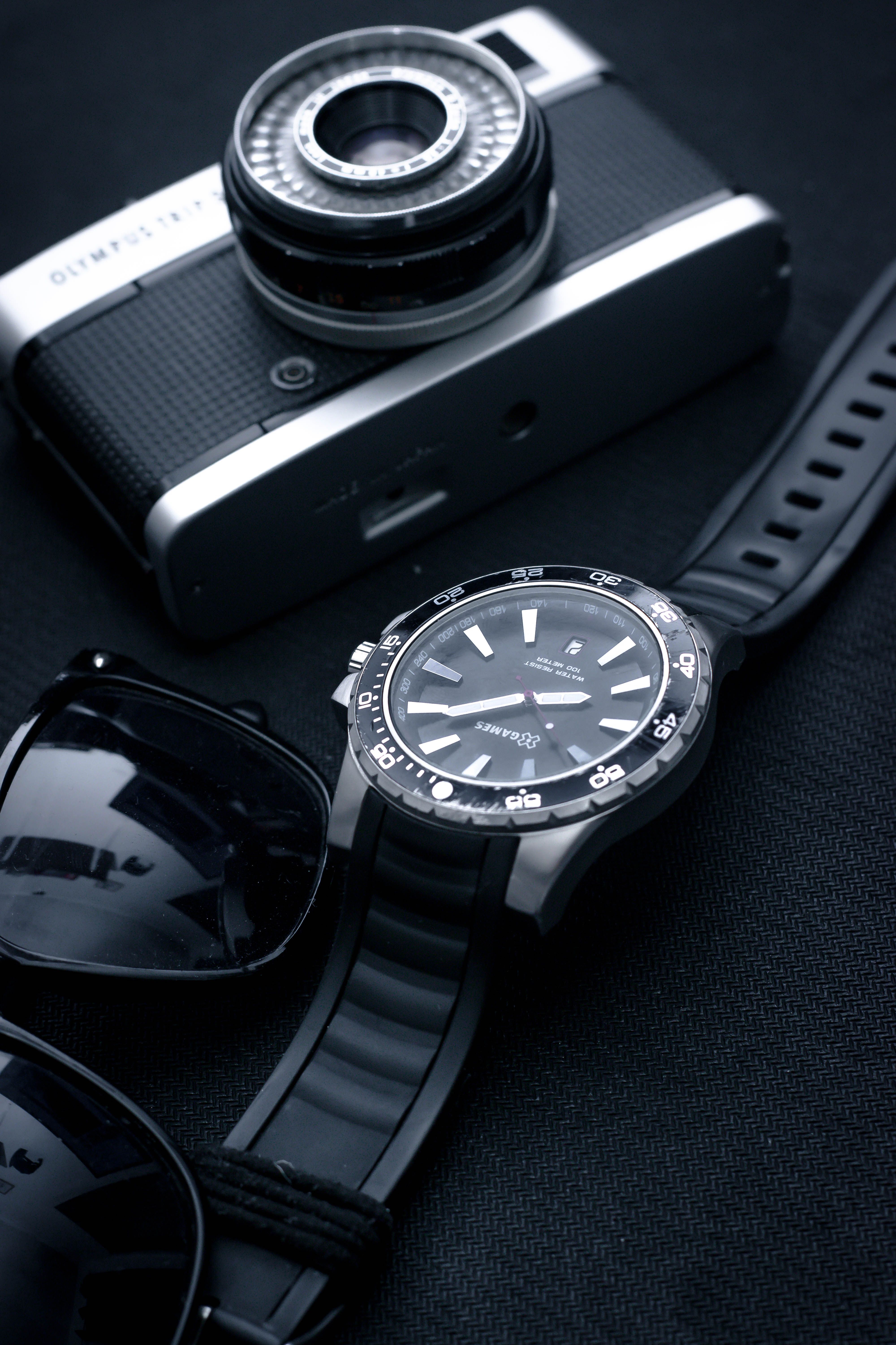 Stylish arrangement featuring a vintage camera, wristwatch, and sunglasses on a dark surface.