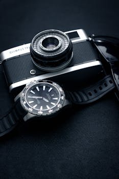 Retro Olympus Trip camera with wristwatch and sunglasses on a dark background, evoking classic photography.