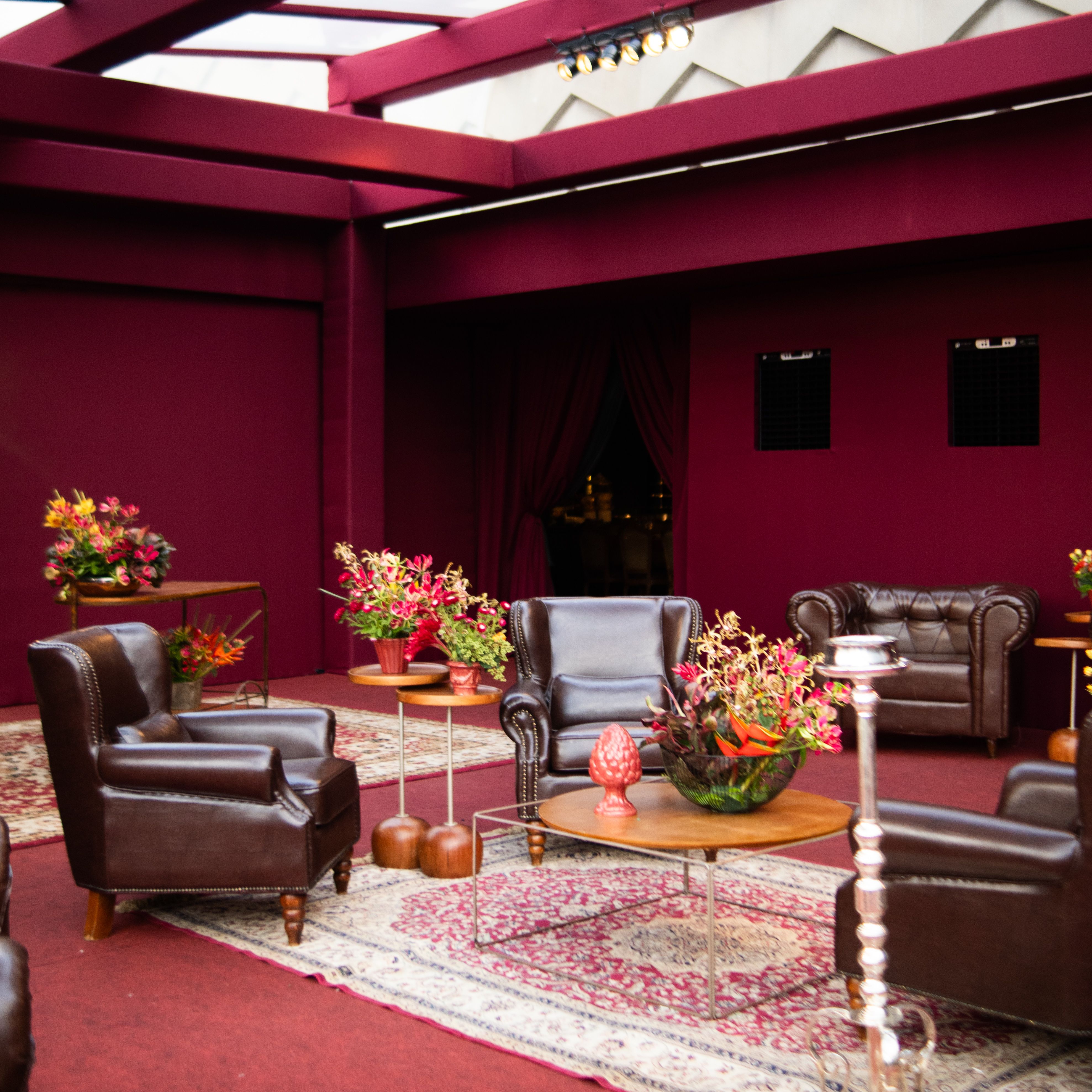 Luxurious indoor lounge featuring brown leather chairs, red walls, and vibrant floral decor.