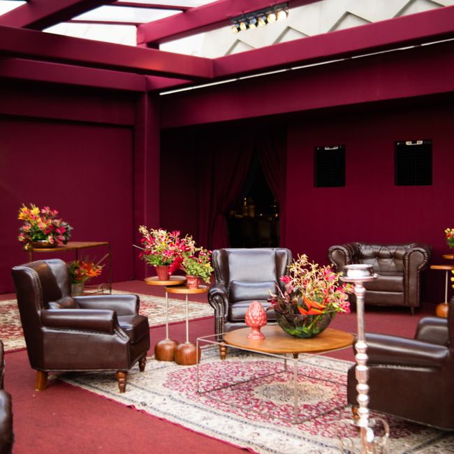 Luxurious indoor lounge featuring brown leather chairs, red walls, and vibrant floral decor.