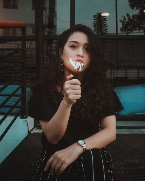 Free Young woman holding a lighter, sitting on stairs outdoors at dusk. Stock Photo