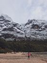冬日白天，白雪皑皑的山脉和郁郁葱葱的森林间，一名徒步旅行者正行走在海滩上