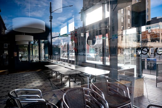 Modern cafe with reflections on glass windows, showcasing empty tables and urban street view.