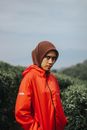 一名头戴头巾、身穿红色夹克的女子站在郁郁葱葱的绿意之中