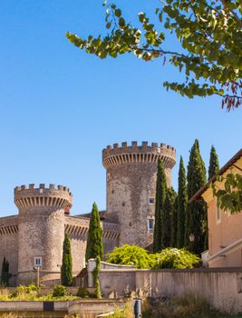 Explore the historic medieval castle with two stone towers surrounded by lush greenery under a clear blue sky.
