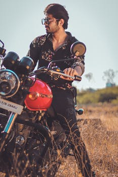 Fashionable man with sunglasses on a Royal Enfield bike in a field, showcasing style and adventure.