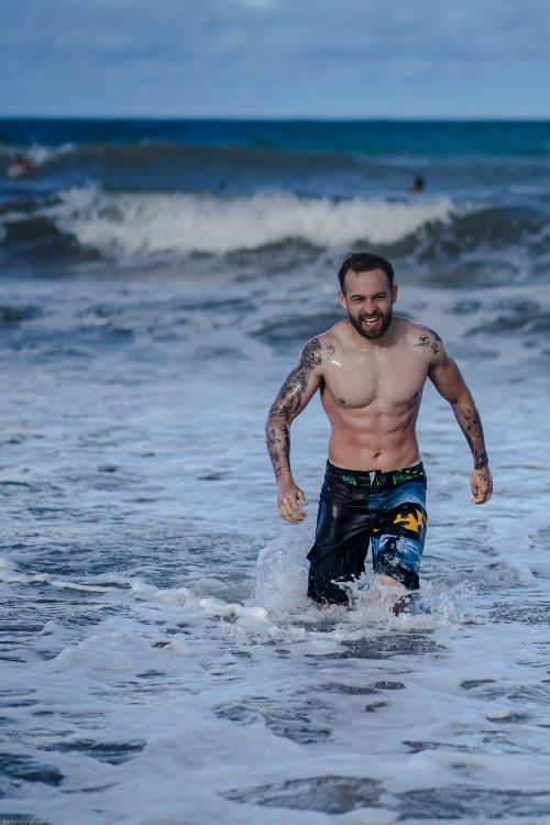 Free A shirtless man with tattoos enjoying ocean waves on a sunny day at the beach in Brazil. Stock Photo