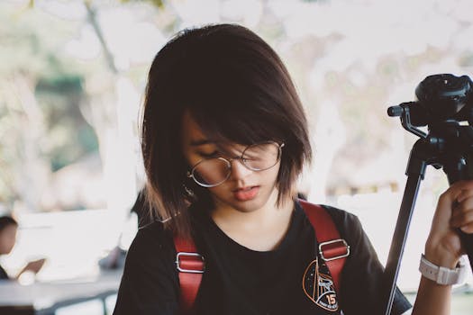 Portrait of a stylish young woman with glasses holding a tripod outdoors.
