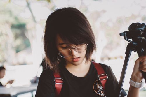 Free Portrait of a stylish young woman with glasses holding a tripod outdoors. Stock Photo