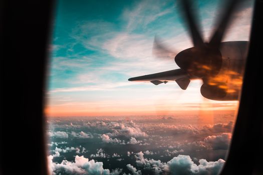 View from a plane window with a propeller against a colorful sunset sky and clouds.