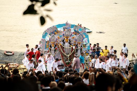 The Durga Puja festival with vibrant idols and a crowd gathered by the riverside in Kolkata, India.