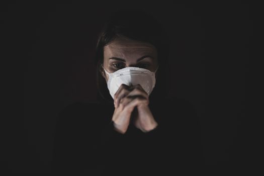 A woman wearing a protective face mask appears concerned in a dark setting, evoking pandemic safety themes.