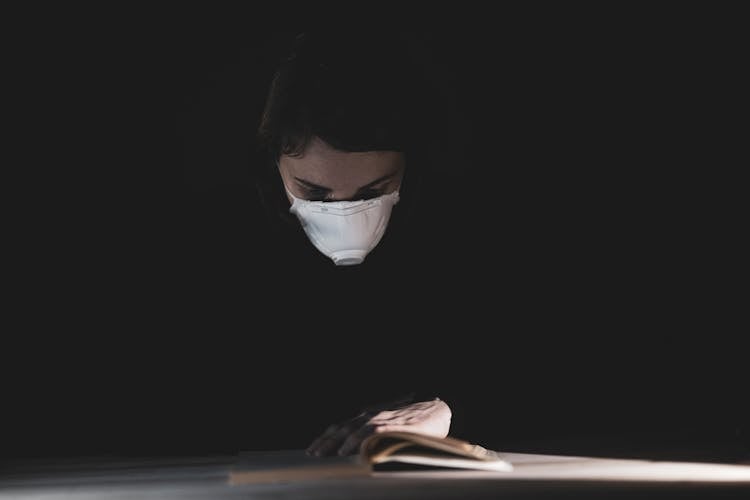 Person In Black Long Sleeve Shirt Wearing N95 Mask While Reading