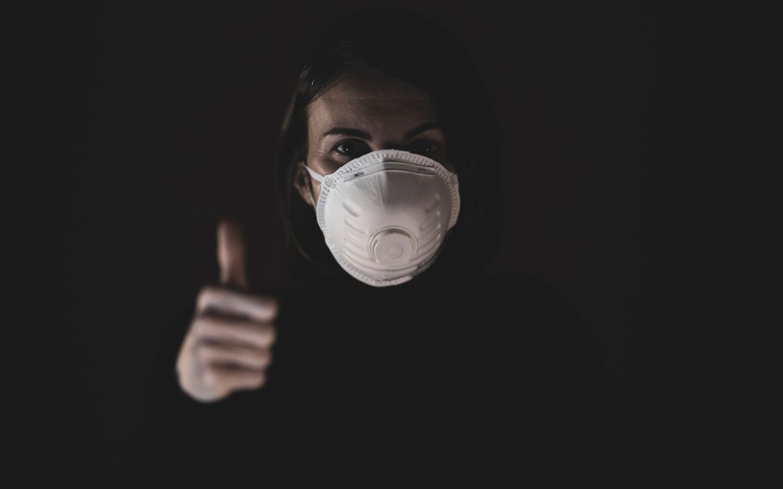 Close-up of a person wearing a white N95 respirator mask against a dark background