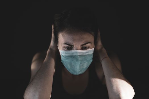 Adult woman wearing a face mask in a dark setting, expressing stress or worry.
