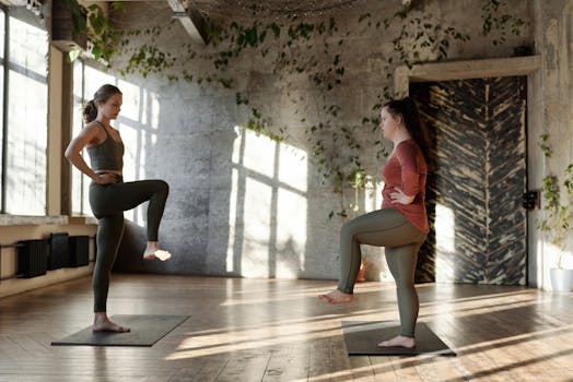 Two women practicing yoga balance poses in a sunlit studio, promoting health and relaxation.