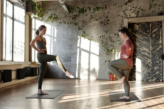 Two women in a sunlit studio practicing yoga with concentration and balance.