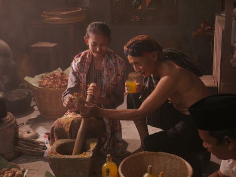 Adults prepare traditional herbal medicine in a cozy indoor setting.