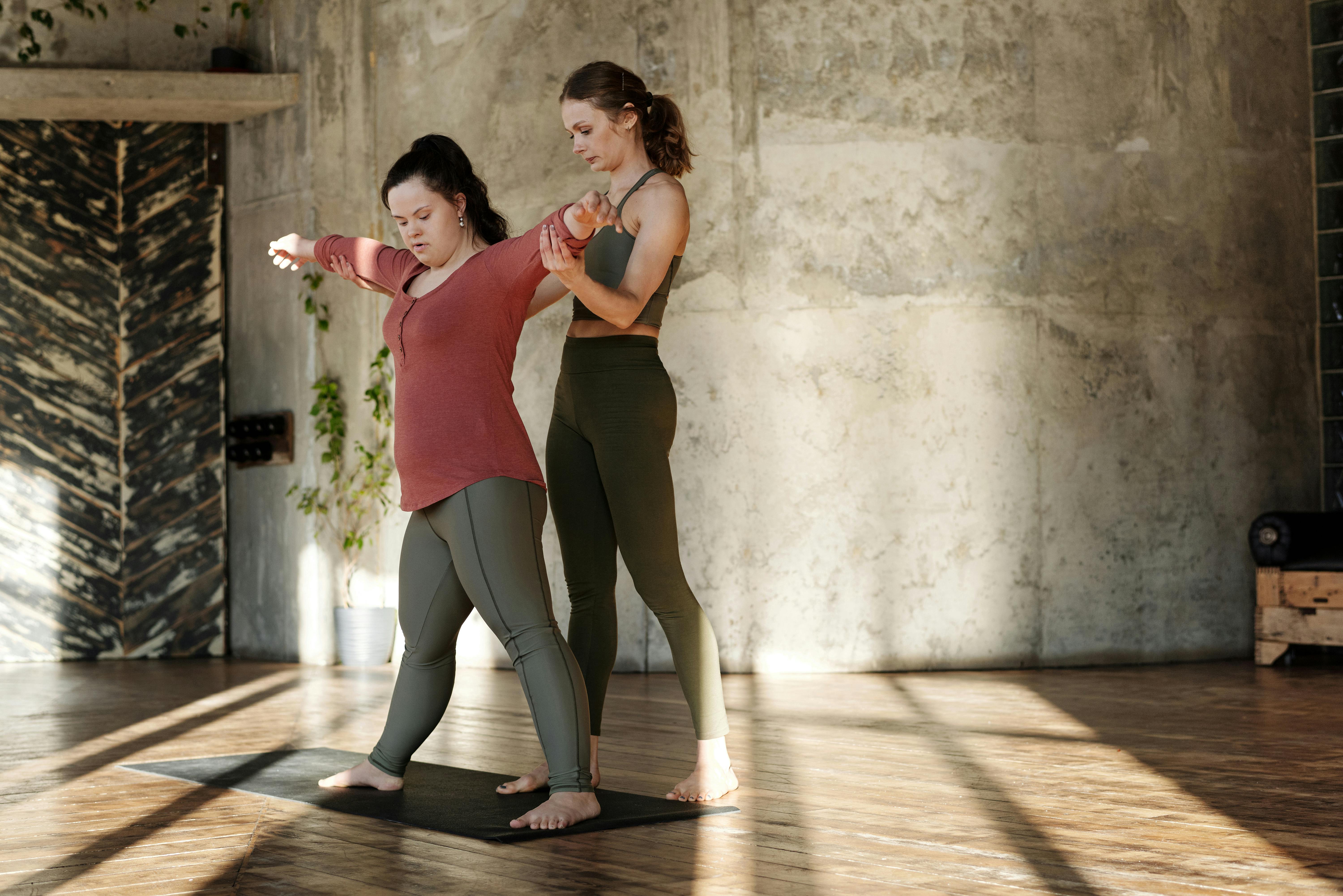 Woman with personal trainer practicing yoga in sunlit room.