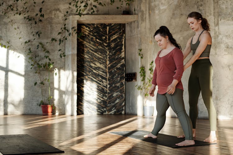 A Yoga Instructor Teaching A Woman In Long Sleeves And Leggings