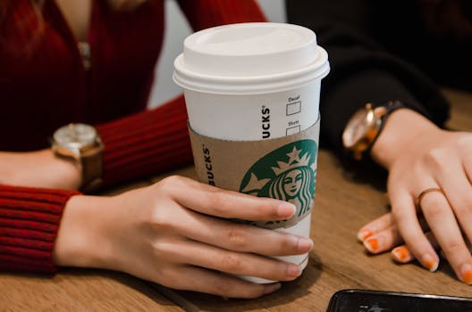 Hands holding a disposable coffee cup with sleeves inside a cafe.