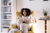 一名妇女在家里读杂志，她的柴犬狗坐在舒适的椅子上