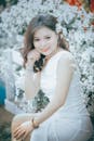一位年轻女子身着白色连衣裙，周围点缀着白花，显得优雅而欢快