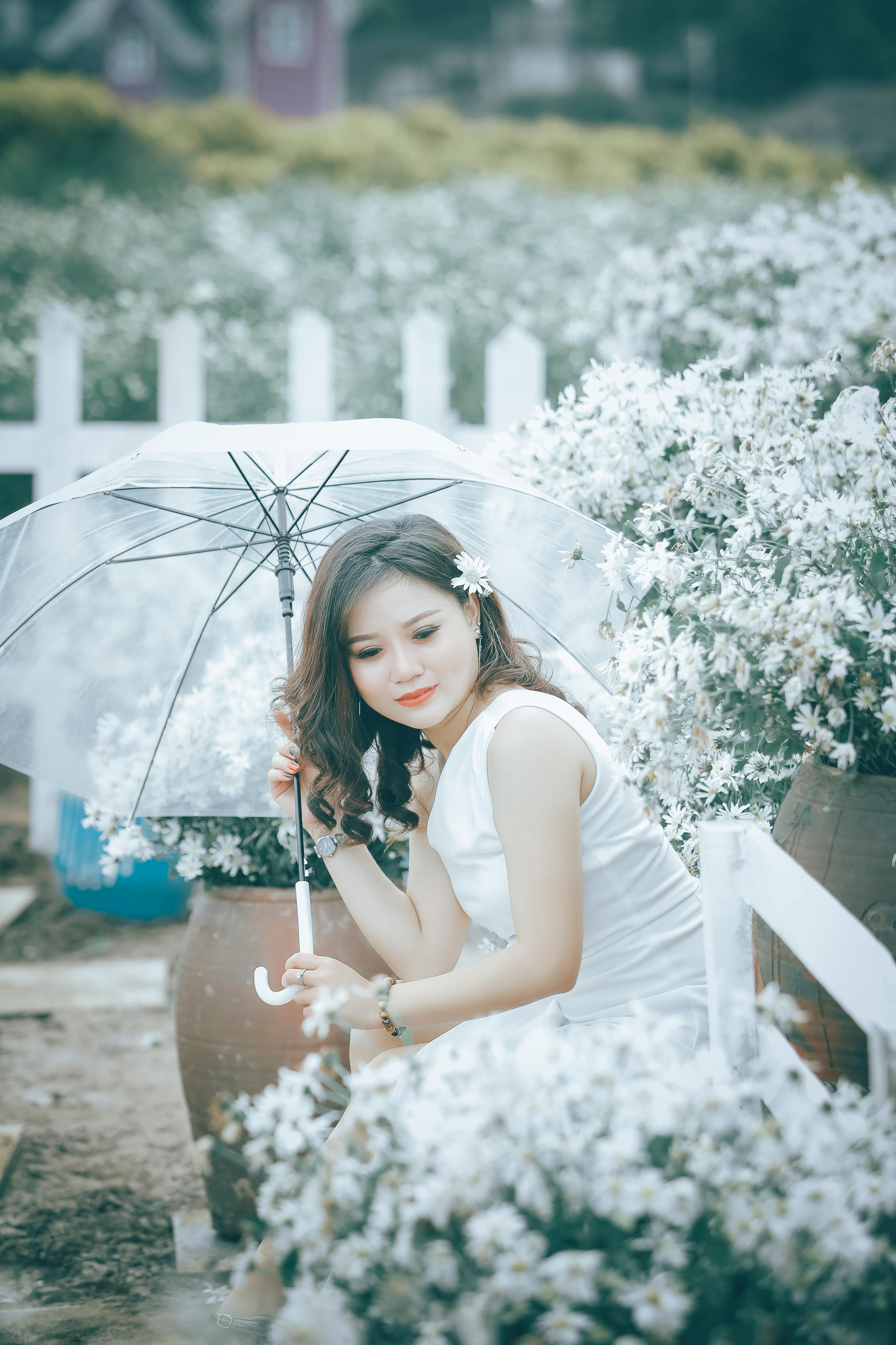 一位优雅的女人手执透明雨伞，静立于白花环绕的宁静花园中