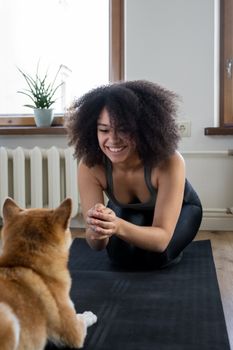 清晨，一位年轻女子在室内的瑜伽垫上与柴犬玩耍，享受舒适的锻炼时光