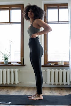 Woman with afro hair doing yoga at home near a window on a sunny morning.