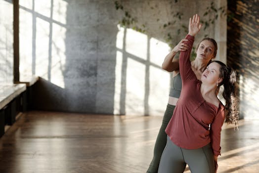 Woman with Down syndrome practicing yoga with trainer in sunlit indoor space.